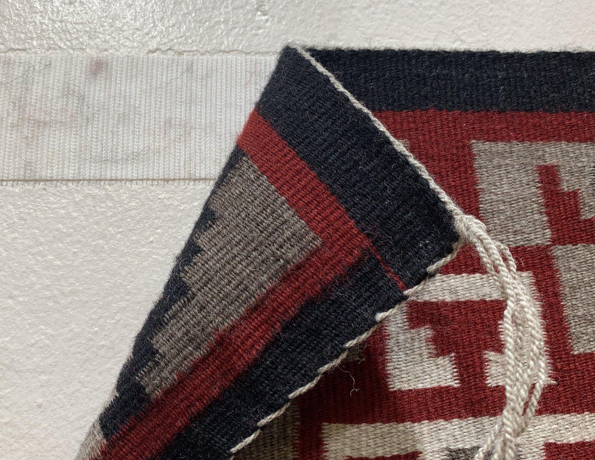 Corner of a Navajo rug folded back to show white Velcro hook tape on the wall behind it
