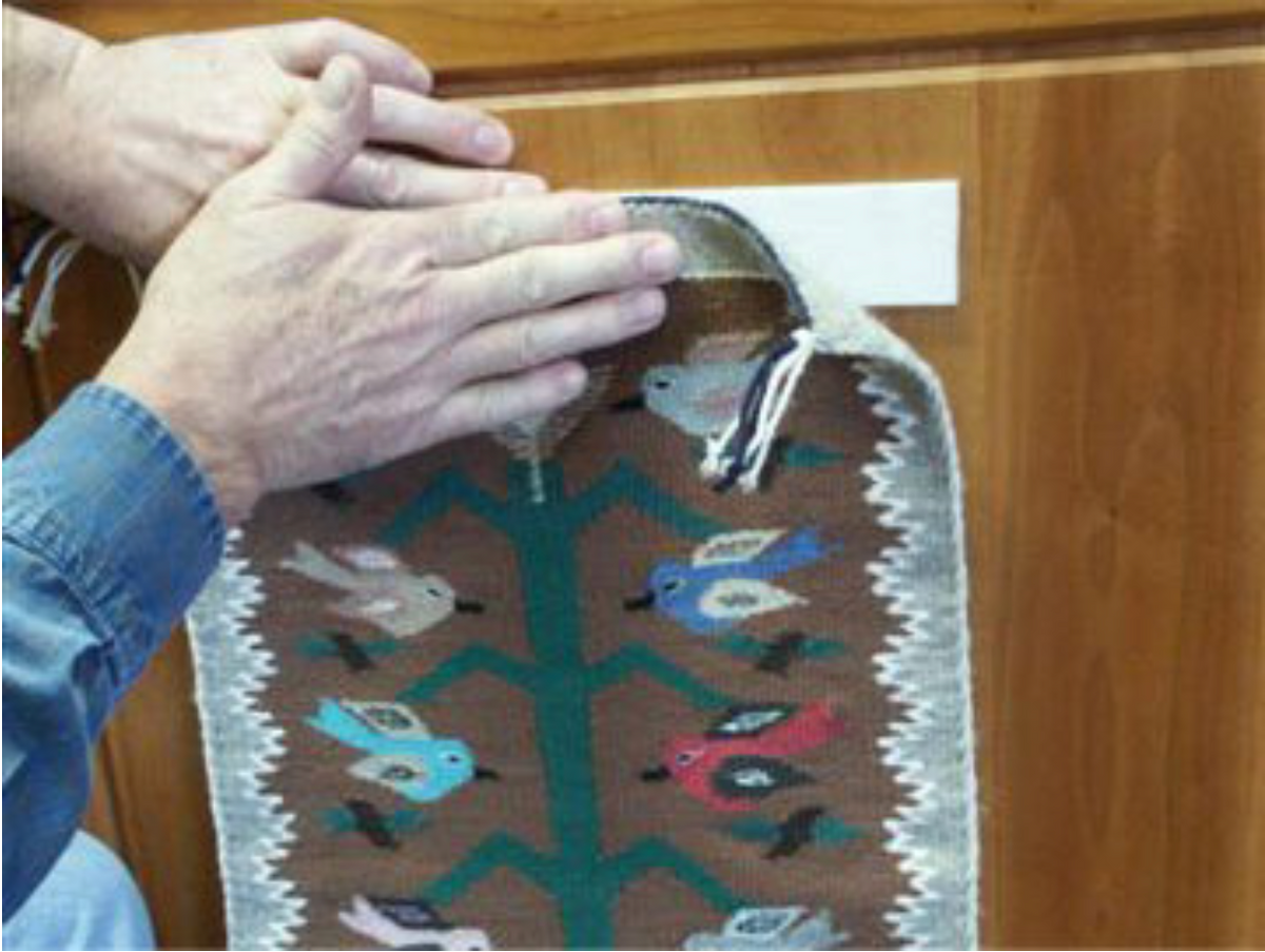Hands pressing the top edge of a Navajo Tree of Life weaving onto the Velcro strip